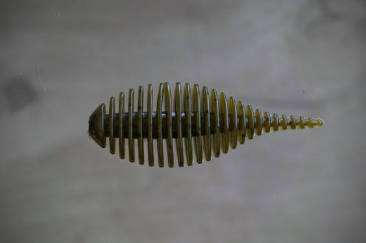 Green pumpkin soft plastic fishing lure with a ribbed body and a tapered tail, shown against a neutral gray background.