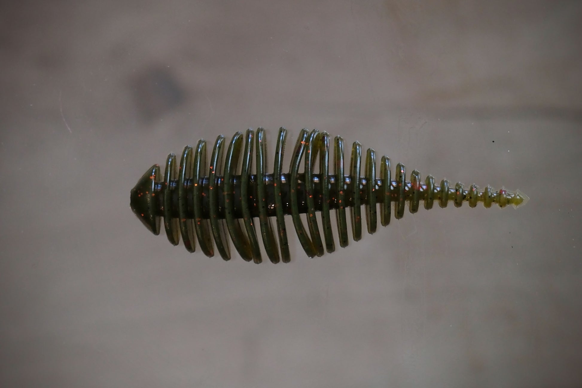 Watermelon with red and black flake fishing lure with a ribbed, segmented body and a tapered tail, shown against a neutral, light gray background.