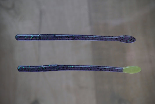 Two soft plastic fishing lures with a dark purple glitter body and a light green spoon tail, shown on a neutral gray background.